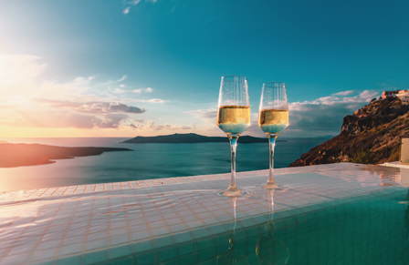 Two wine glasses sitting by the edge of a pool at sunset
